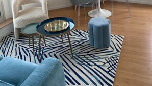 A modern living room with a round white table, a blue sofa, and a patterned rug.