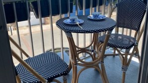 A balcony with two tables and two chairs, a railing, and a house in the background.