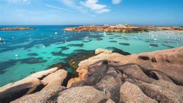 A coastal landscape with clear blue waters, rocky formations, and boats.