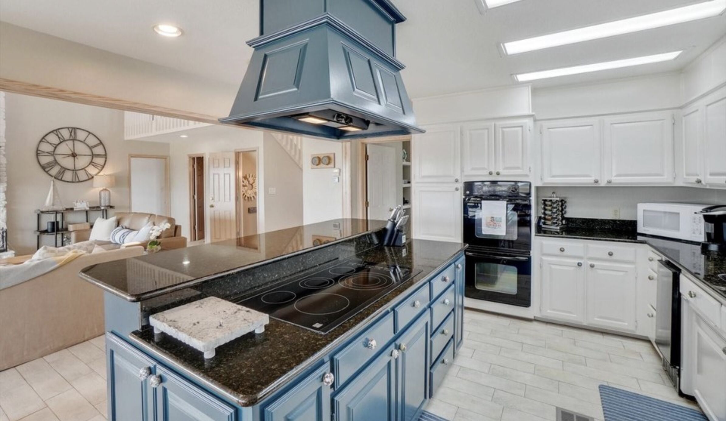 A modern kitchen with a central island, built-in oven, and white cabinetry.