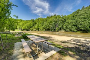 A picnic table with benches in a park with a river and dense forest in the background. - West Jefferson Vacation Rental Near River (West Jefferson)