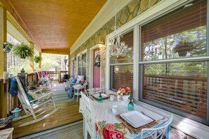 A covered porch with rocking chairs, a table set for dining, and large windows with blinds. - West Jefferson Vacation Rental Near River (West Jefferson)