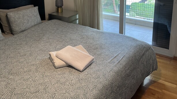 Ein Schlafzimmer mit einem großen Bett, einem Nachttisch, einer Lampe und Blick auf einen Balkon.
