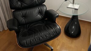 Ein schwarzer Bürostuhl mit Armlehnen, ein Glastisch mit schwarzem Fuß und eine weiße Lampe auf dem Tisch.