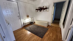 Ein Zimmer mit Holzboden, einer weißen Tür, einem weißen Schreibtisch mit Lampe, einer Bank und einem Bild an der Wand.