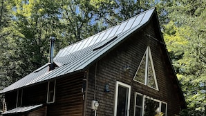 Une cabane en bois avec un toit en pente, une cheminée et une véranda à l’avant.