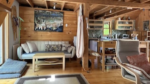 L’intérieur d’un chalet en bois chaleureux et accueillant, avec un canapé, une table à manger, un coin cuisine et un grand tableau accroché au mur.