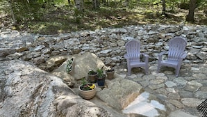 Une terrasse en pierre avec deux fauteuils Adirondack et des plantes en pot.