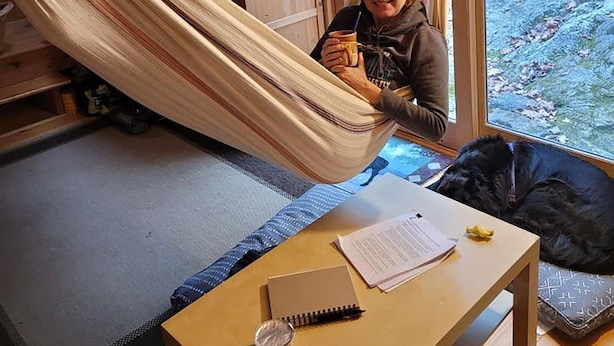 Une personne se détend dans un hamac à l’intérieur d’une cabane en bois, avec vue sur une zone boisée.