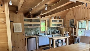 Une cuisine rustique aménagée dans une cabane en bois, avec un réfrigérateur encastré, un évier et une table à manger en bois.