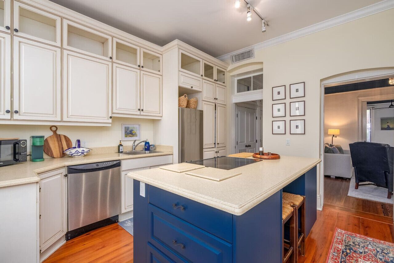 A modern kitchen with white cabinetry, a blue island, stainless steel appliances, and a wooden floor.