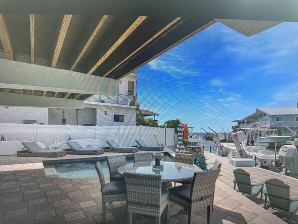 An outdoor pool area with lounge chairs, a table, and a view of boats and houses.