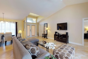 A spacious living room with a sofa set, a coffee table, and a TV mounted on the wall. - Lovely Home with Canal View, Heated Pool, Boatlift, Stunning Sunsets (Cape Coral)