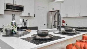 Une cuisine moderne avec des meubles blancs, un réfrigérateur en acier inoxydable et un plan de travail noir.