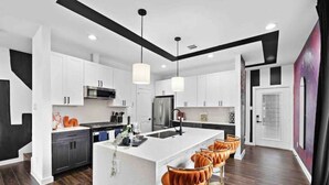 Une cuisine moderne avec des meubles blancs, un îlot central doté de tabourets de bar et un plafond noir qui crée un effet décoratif.