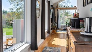 Una habitación amplia con grandes ventanales, piso de madera, cafetera y vistas al exterior.