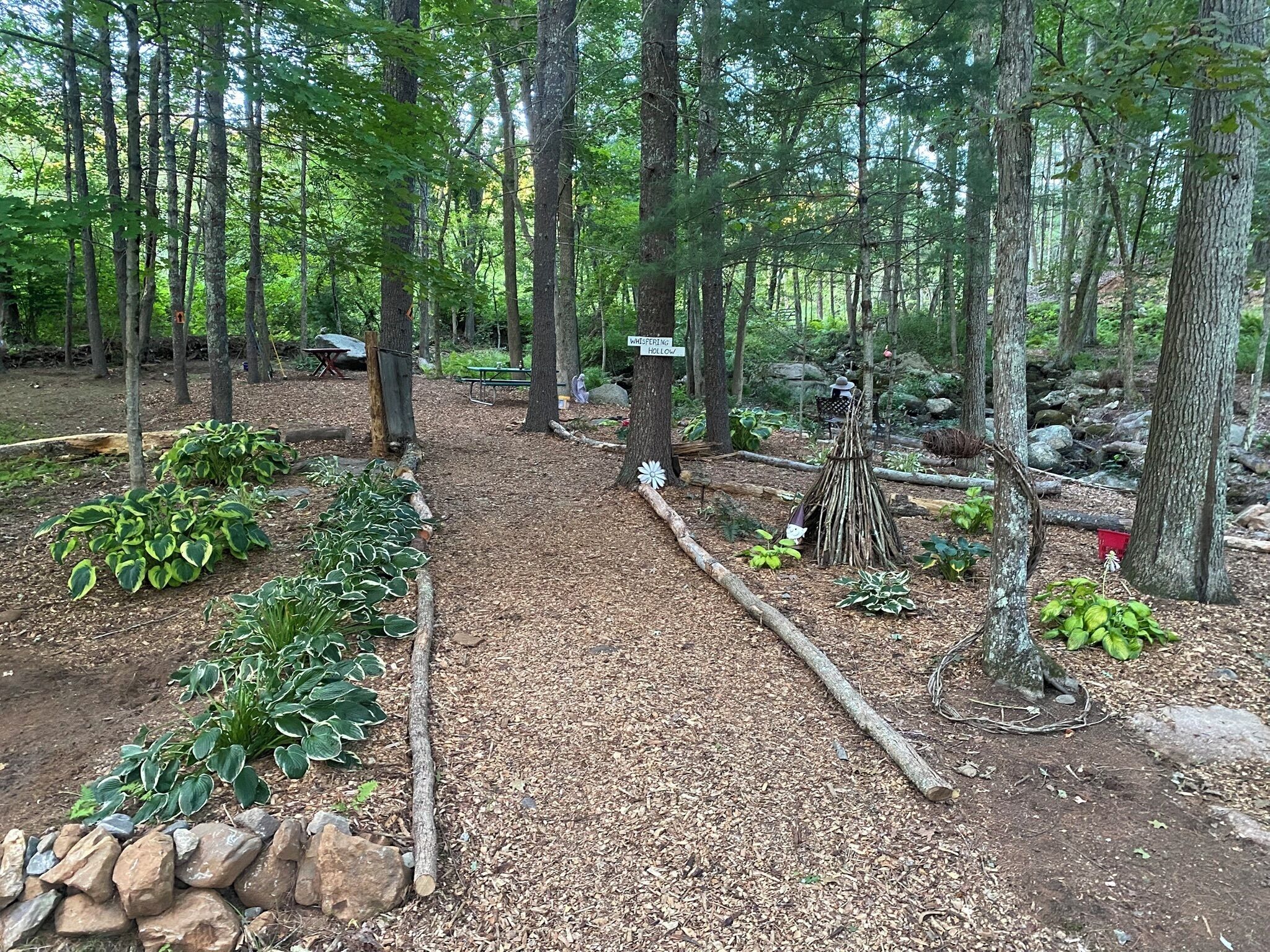 A forested area with a dirt path, a small wooden structure, and a sign indicating 'Whispering Hollow'.