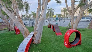Un parque con césped artificial, árboles y juegos infantiles.