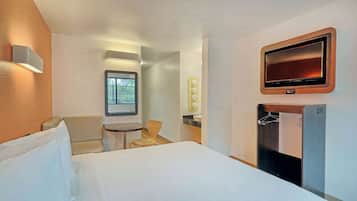 A hotel room with a bed, a desk, a chair, a TV, and a wardrobe.