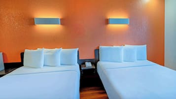 Habitación de hotel con dos camas, ropa de cama blanca, una mesita con un teléfono y luces fijadas a la pared.
