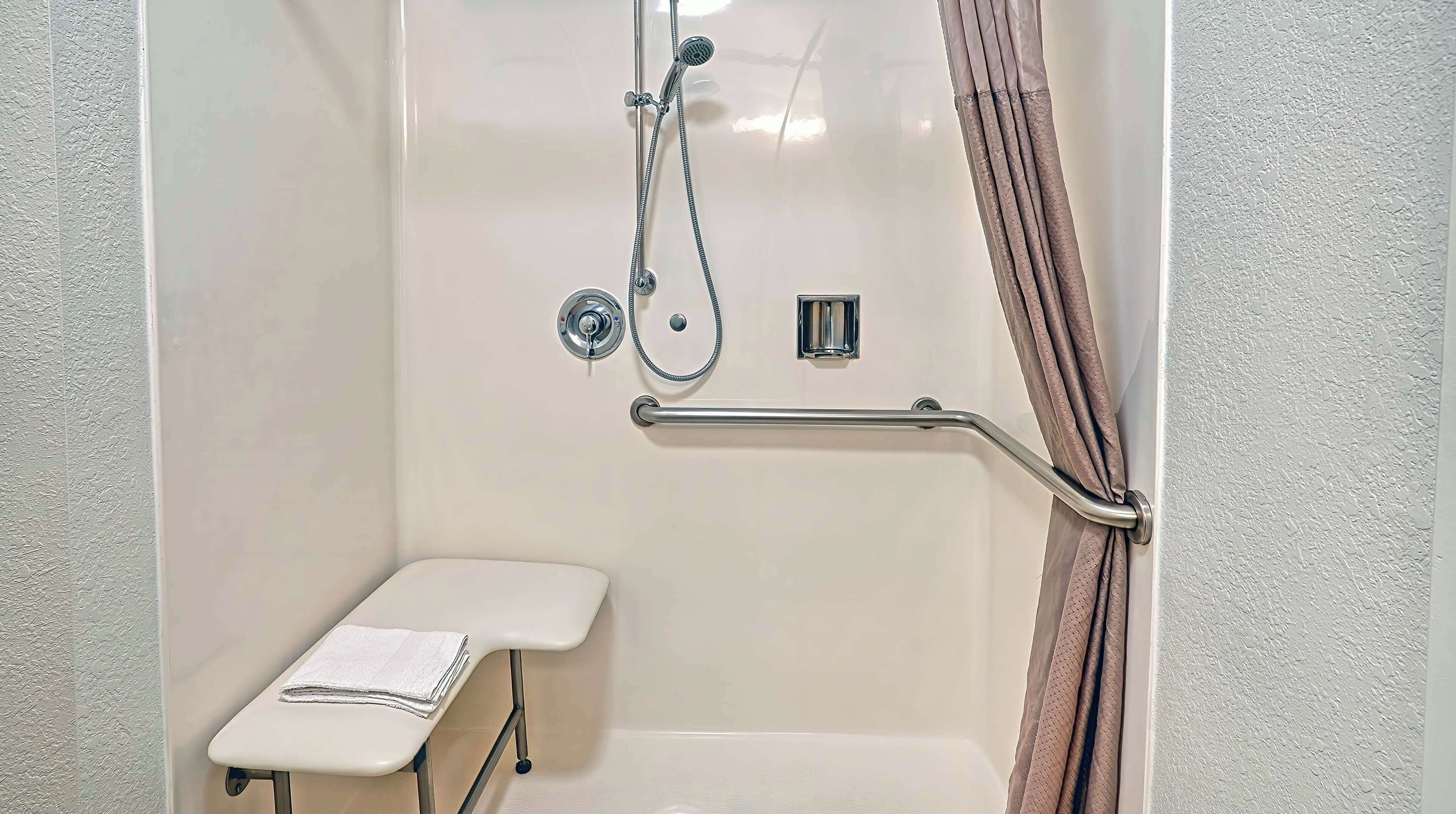A shower area with a grab bar, a small bench, and a showerhead.