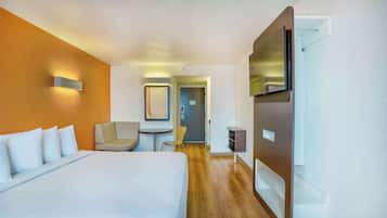 A hotel room with a bed, a chair, a desk, a TV, and a door leading to a bathroom.