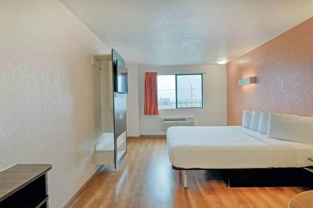 A hotel room with a bed, a TV, a window, and a door.