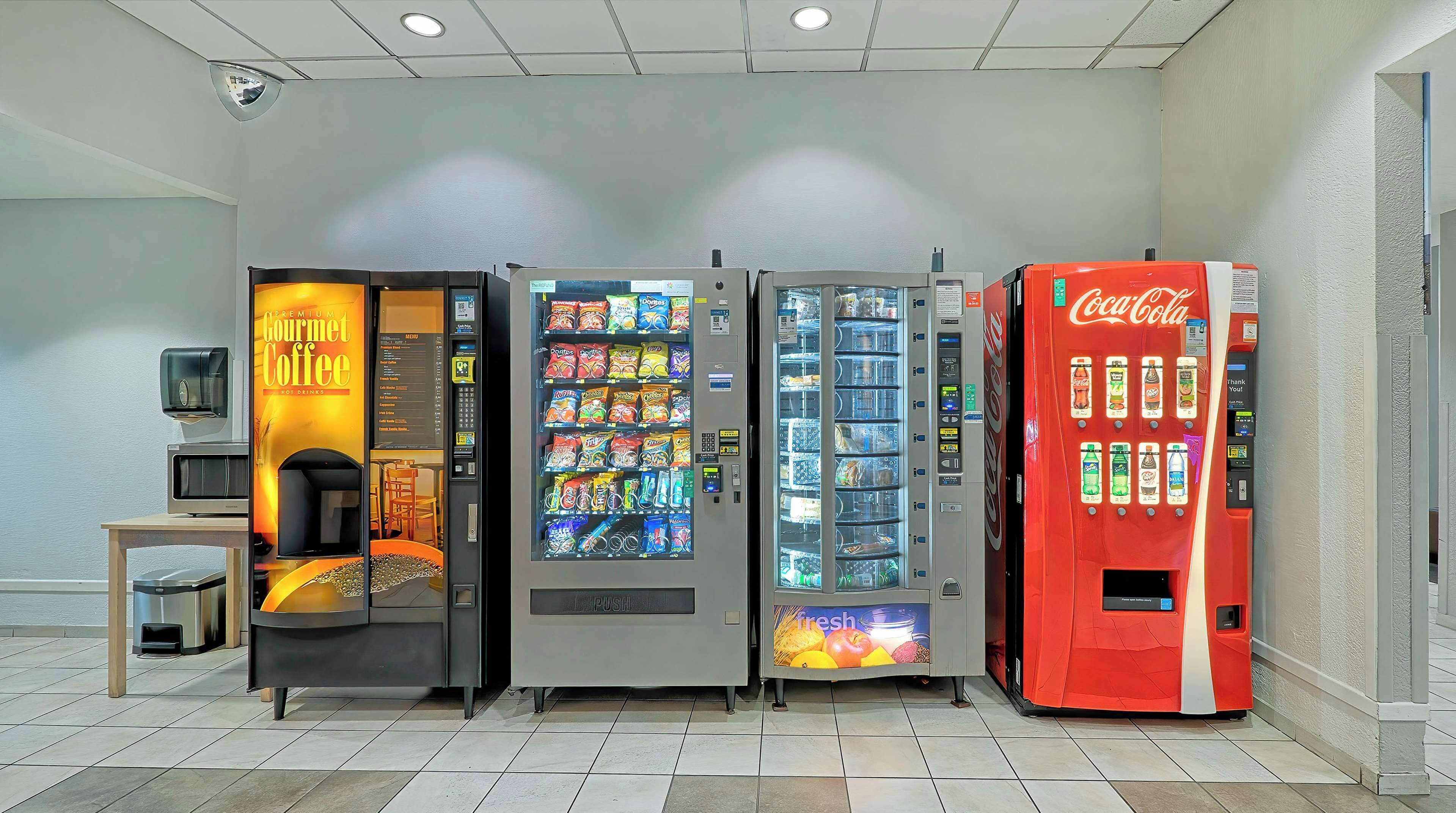 Una fila de máquinas expendedoras, incluyendo una de café, dispensadores de aperitivos y una máquina de Coca-Cola.
