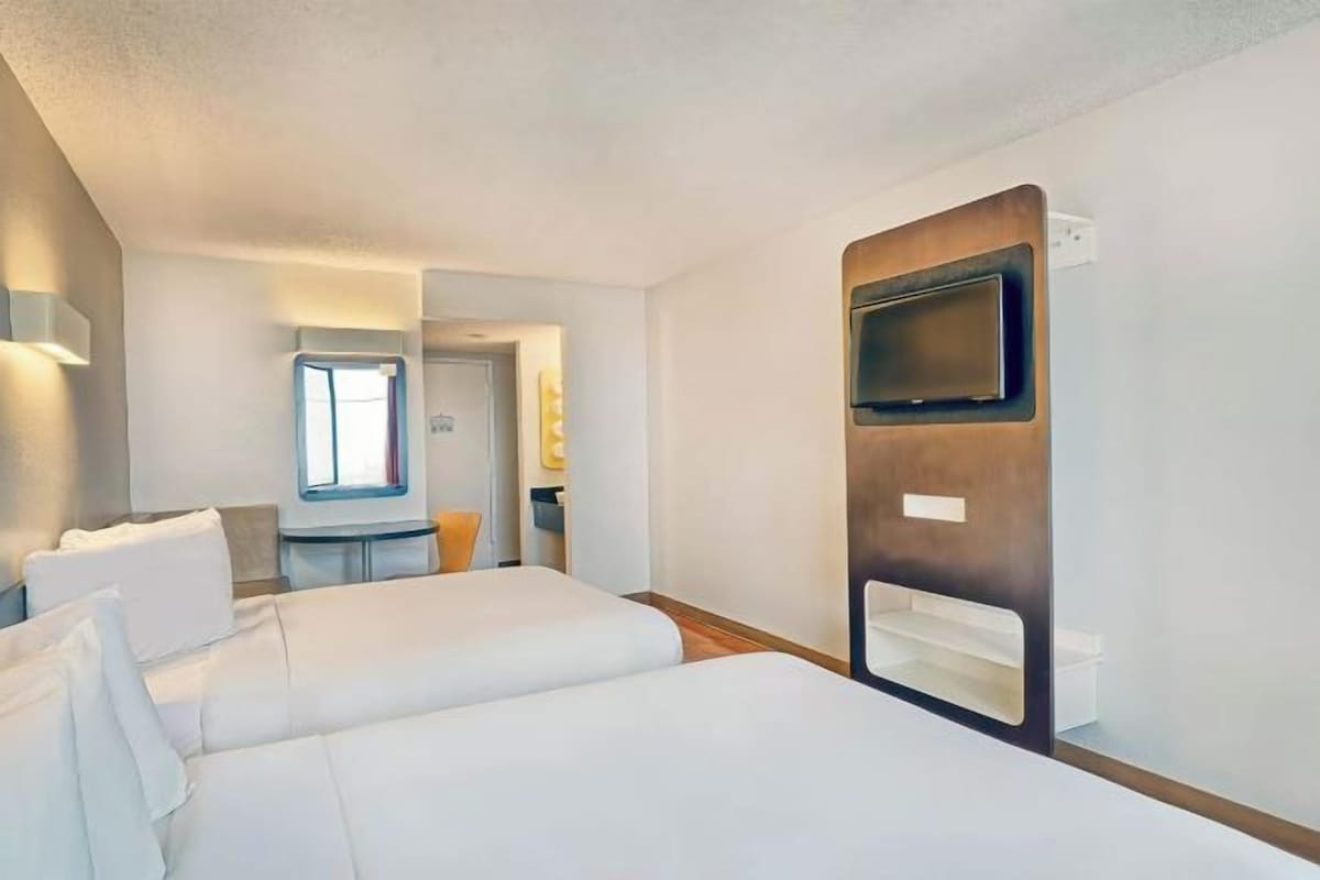 A hotel room with two beds, a TV, a desk, and a window.