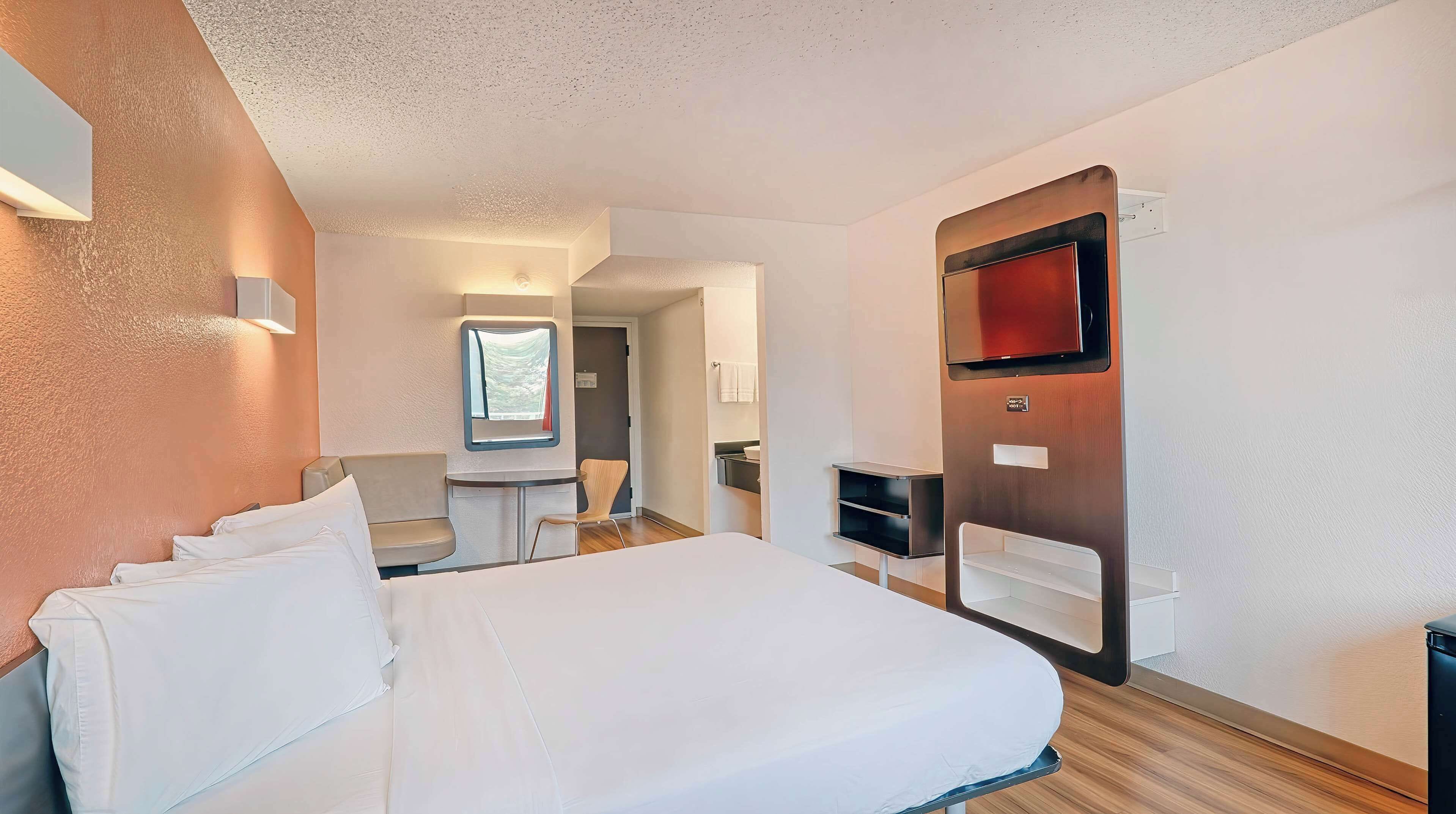 Une chambre d’hôtel avec un grand lit, un téléviseur fixé au mur, un petit bureau et une fenêtre.
