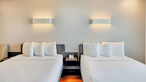 Habitación de hotel con dos camas, ropa de cama blanca, mesita de noche con teléfono e iluminación empotrada.