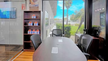 Une salle de conférence équipée d’une grande table, de chaises, d’une machine à café et offrant une vue sur un jardin grâce à de grandes fenêtres.
