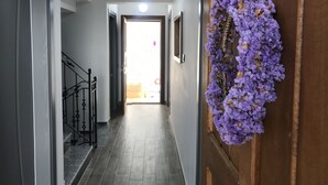 A hallway with a wooden door on the right, a staircase on the left, and a view into a room at the end. - Demirtaş Pansiyon (Bozcaada)