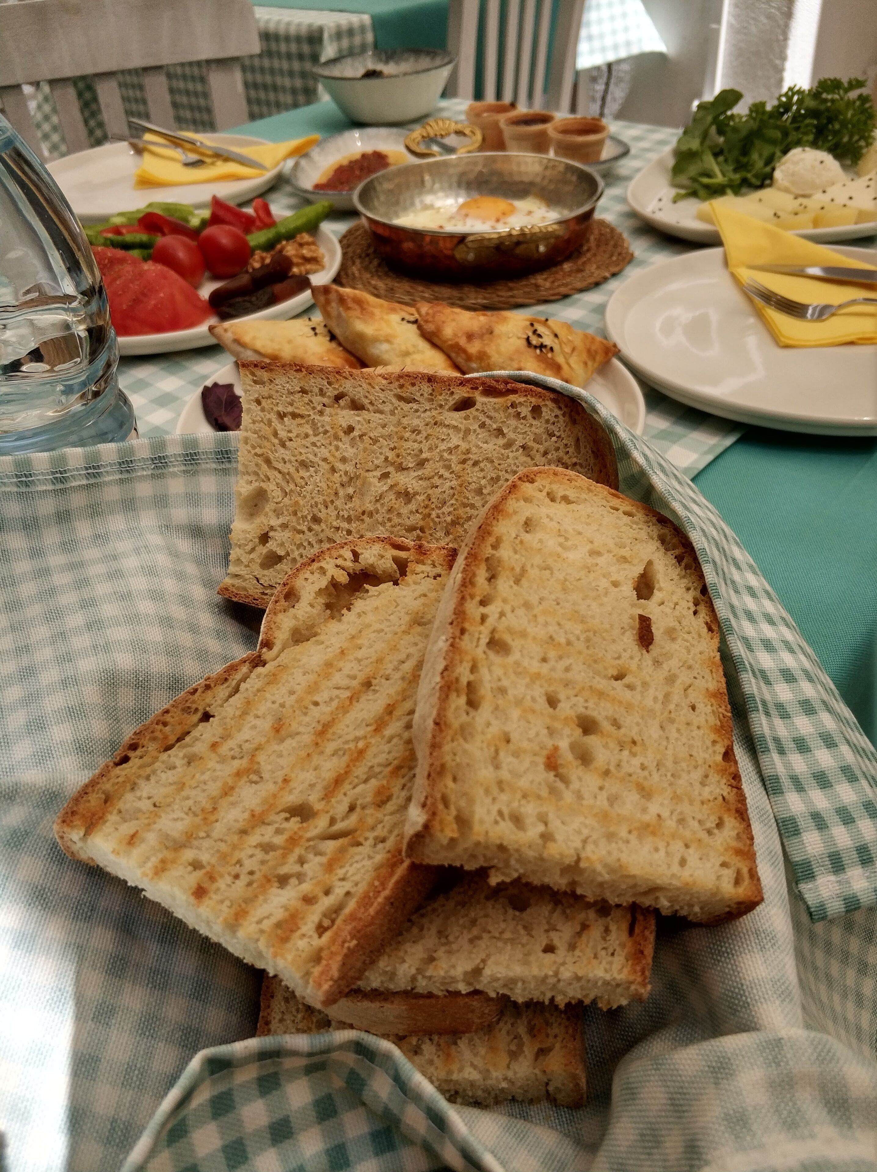 A table with a checkered tablecloth, a glass of water, and various food items including bread, vegetables, and a bowl of soup.