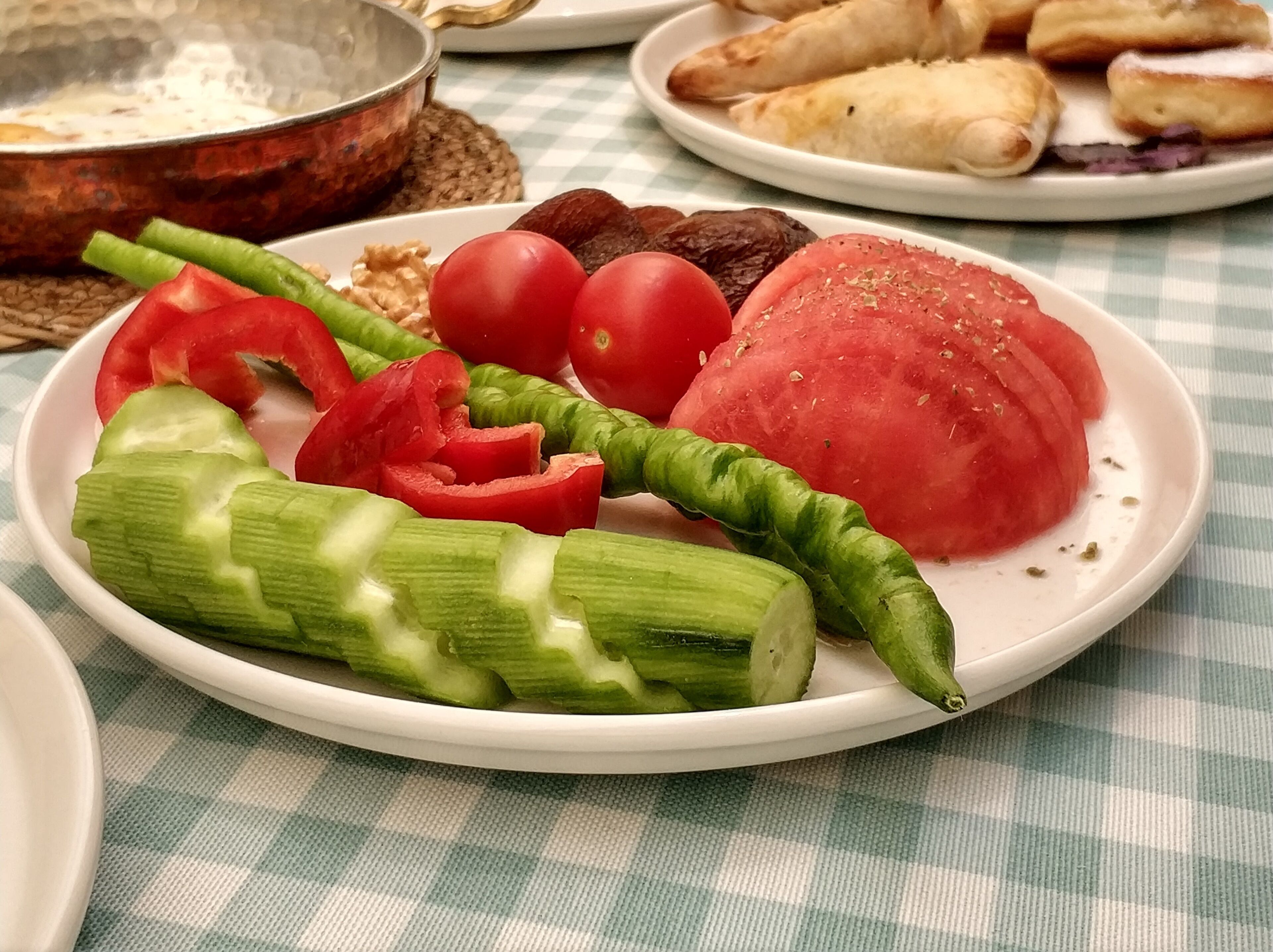 A plate with sliced tomatoes, cucumbers, and a green vegetable, possibly a pepper, on a checkered tablecloth.