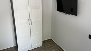 A white wardrobe with two doors and a flat-screen TV mounted on the wall. - Demirtaş Pansiyon (Bozcaada)