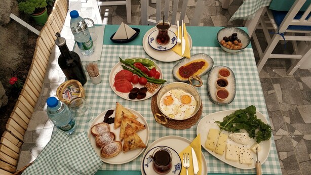 A table set with various dishes including eggs, bread, and vegetables, with a checkered tablecloth and outdoor seating. - Demirtaş Pansiyon (Bozcaada)