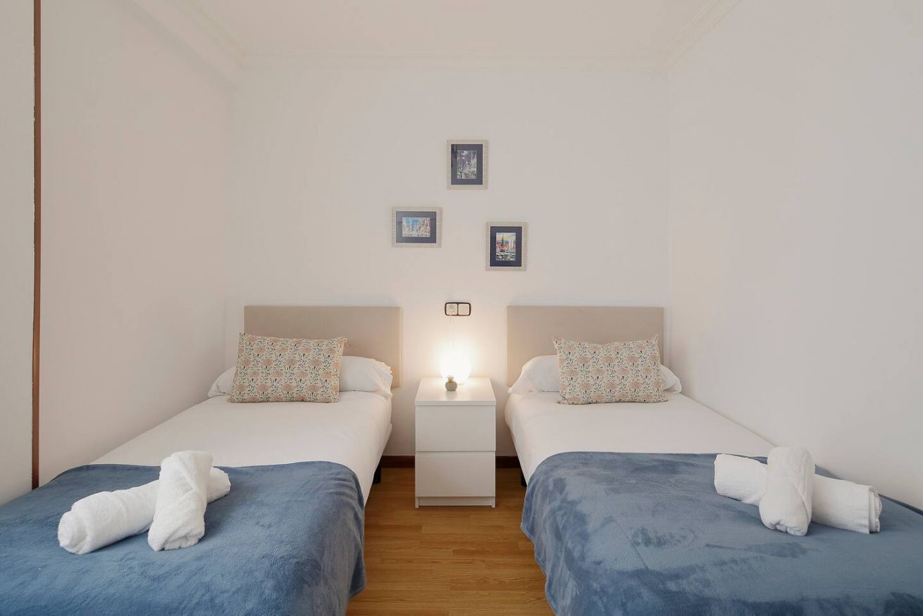 A twin bedroom with two beds, a nightstand, and a wall-mounted light.