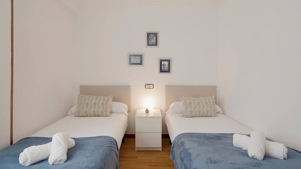Une chambre double avec deux lits, une table de chevet et une lampe fixée au mur.