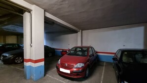 Un parking avec des piliers en béton, une voiture rouge et une voiture noire qui y sont garées.