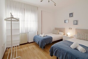 A hotel room with two beds, a radiator, a coat rack, and a bedside table with a lamp.