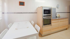 Une cuisine avec une table blanche, deux chaises, un four à micro-ondes, un four et une horloge au mur.
