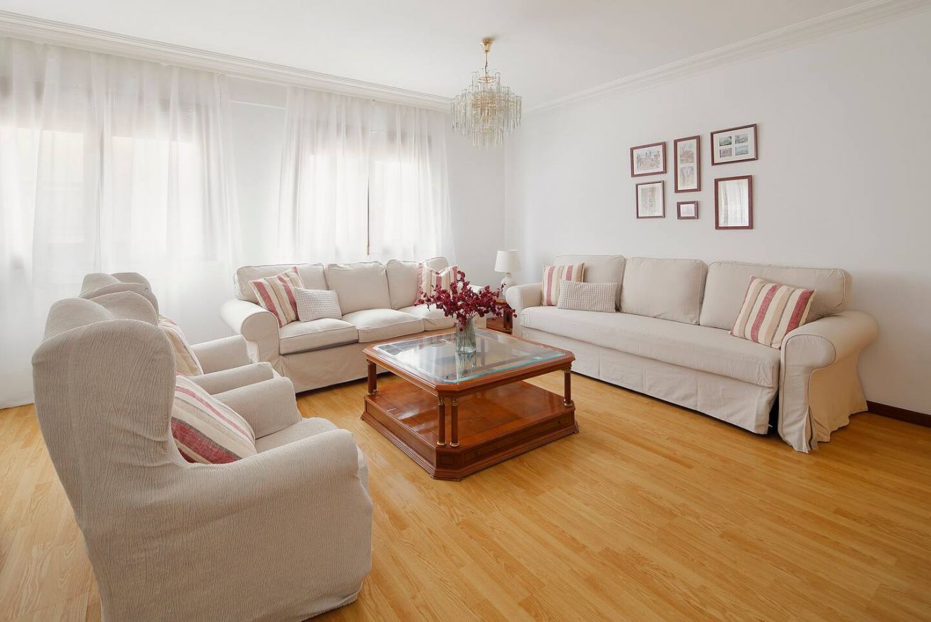 A living room with a sofa set, a glass coffee table, and a chandelier.