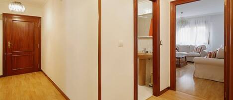 Ein Flur mit Holzboden, einer Holztür und einem Spiegel, der ein Wohnzimmer mit Sofa und Fenster wiederspiegelt.