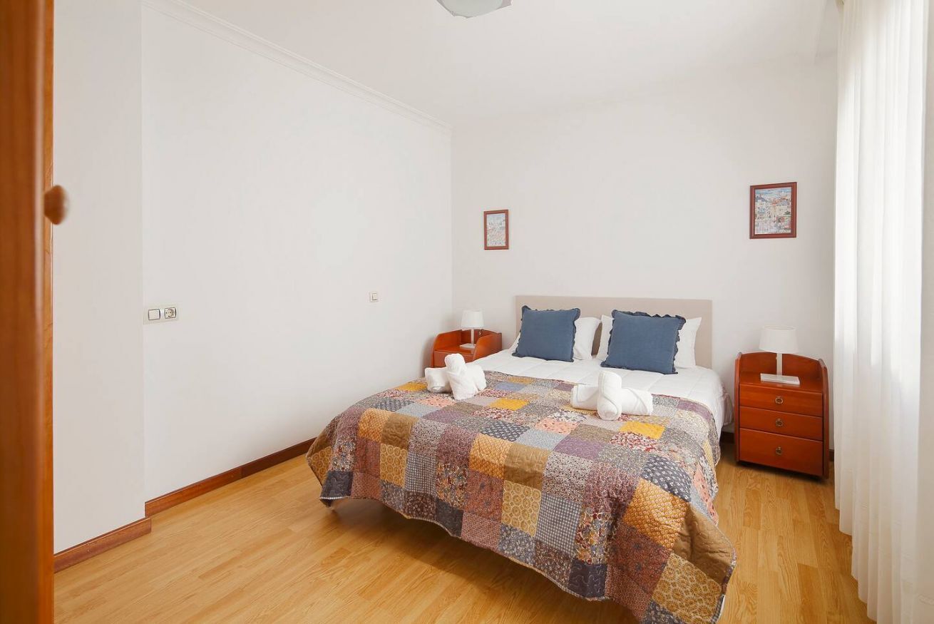 A bedroom with a bed, two bedside tables, a quilt, and a nightstand.