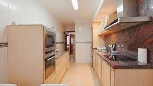 Une cuisine moderne dotée d’appareils électroménagers en acier inoxydable, d’un pare-feu en marbre et d’un coin repas avec une table et des chaises blanches.