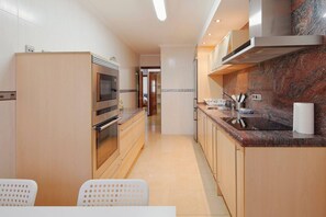 A modern kitchen with stainless steel appliances, a marble backsplash, and a dining area with a white table and chairs. - 174A Apartment in San Lorenzo by R2R Consulting (Gijón)