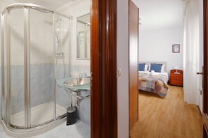 A hotel bathroom with a glass shower enclosure, a glass sink, and a wooden floor.