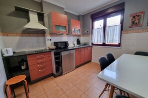 Cocina compacta con microondas, tostadora y lavavajillas. Hay una mesa de comedor con sillas y un ventanal con cortinas.