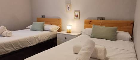 Habitación de hotel con dos camas, cada una con cabecero de madera, ropa de cama blanca y una mesita de noche con lámpara.